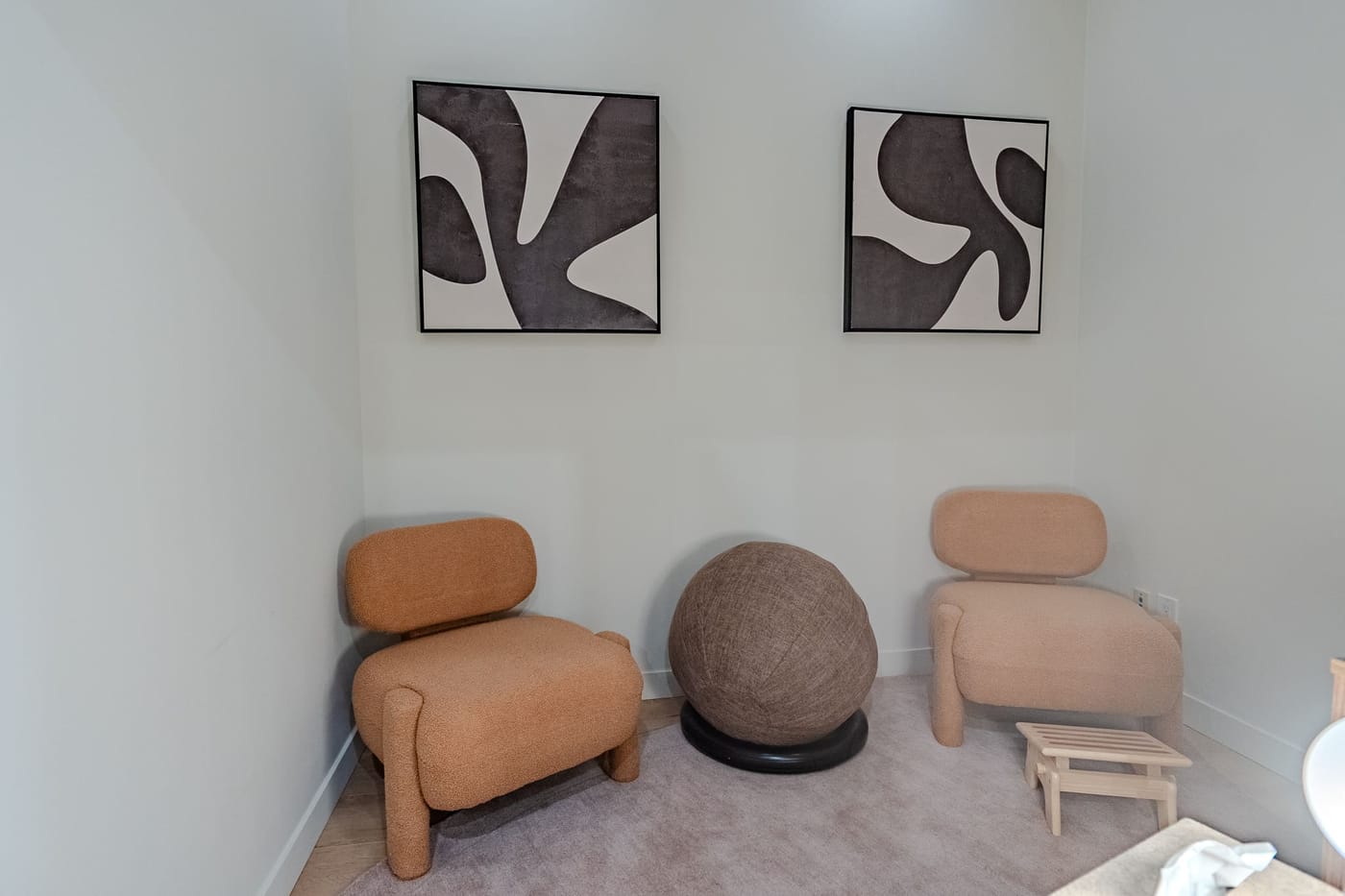 A quiet seating corner with boucle chairs, abstract art, and a therapy ball