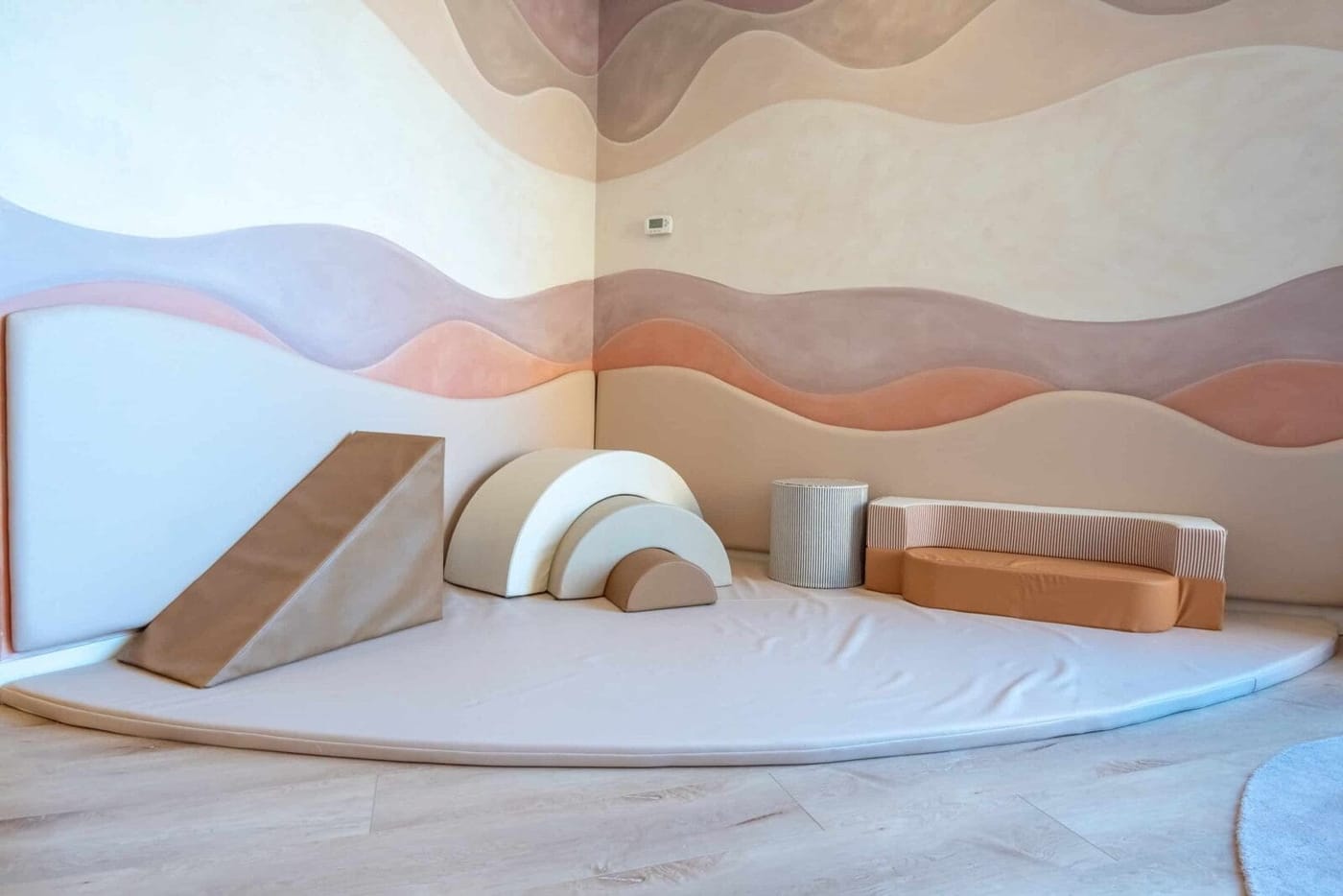 A sensory soft-play corner with foam shapes set against a warm, wave-painted wall