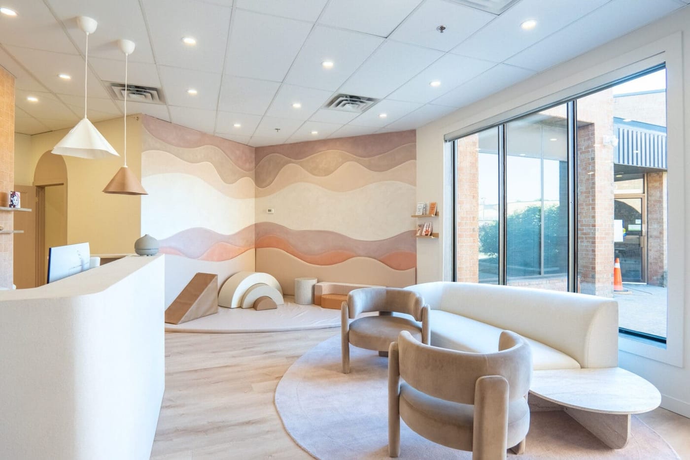 The reception and waiting area, with a curved sofa and a soft-play nook beneath a warm wave mural